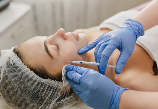 یک خانم در حال انجام بوتاکس بر روی صورت در ناحیه گونه و زیر چشم است و پزشکی با دستکش آبی رنگ سرنگ حاوی بوتاکس را روی صورت او گذاشته است . بیمار بر روی تخت ریلکس خوابیده است