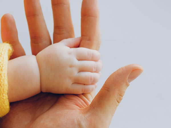 داخل عکس یک دست فرد بالغ و یک دست نوزاد وجود دارد. این دو فرد دستان همدیگر را گرفته اند. پوست دست نوزاد صاف و روشن می باشد. اما پوست دست فرد بالغ کمی تیره تر است.