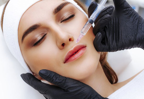 یک خانم در حال تزریق ژل به ناحیه حاشیه لب هایش توسط پزشک می باشد . زمینه تصویر سفید ، دستکش پزشک مشکی و تصویر بیمار بصورت بسته می باشد