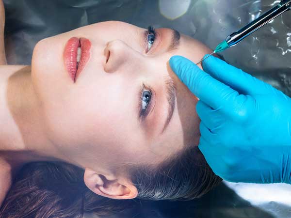 تصویر یک خانم در حالت خوابیده روی تخت در حال تزریق بوتاکس به داخل پوست پیشانی . دستکشهای دکتر آبی رنگ می باشند .