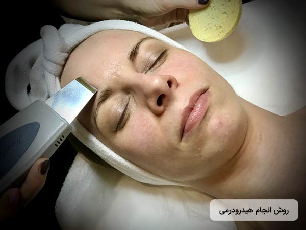 يک خانم روي تخت دراز کشيده است و چشمان خود را بسته است. پزشک درحال زيباسازي و آبرساني به پوست صورت او با استفاده از روش هيدرودرم ابريژن مي باشد.